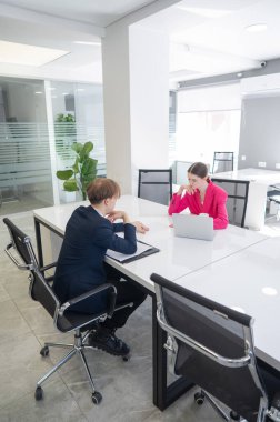 Kadın ve erkek ofiste otururken konuşuyorlar.