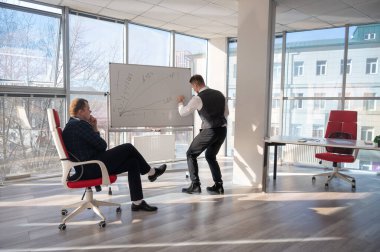 Beyaz bir kurulda iş tartışan iki beyaz adam.