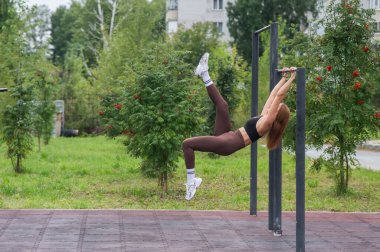 Genç bir kadın açık havada yatay barlarda egzersiz yapıyor.