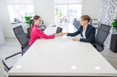 Beyaz erkek ve kadın ofiste selamlaşıp el sıkışıyor.