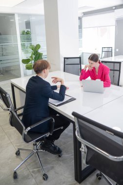 Kadın ve erkek ofiste otururken konuşuyorlar.