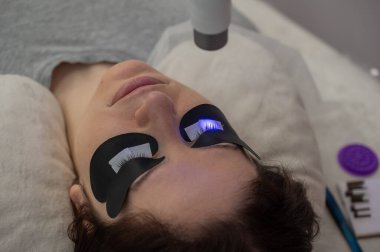 Kirpik uzatma prosedüründen geçen bir kadın ultraviyole lamba kullanıyor.