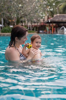 Beyaz kadın tatilde havuzda yüzerken oğlunu kucağına aldı