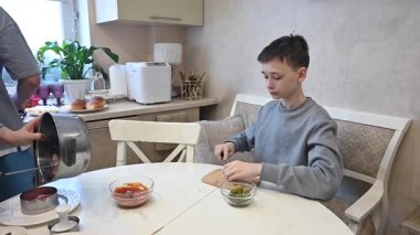 Orta yaşlı beyaz kadın iki oğluyla hamburger pişiriyor.