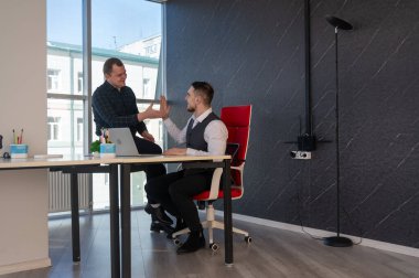 Beyaz adam çalışma masasında durmuş iş hakkında konuşuyor.