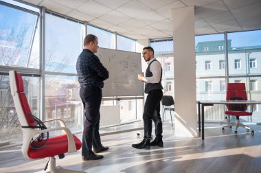 Beyaz bir kurulda iş tartışan iki beyaz adam.