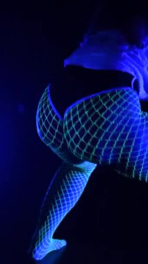 Genç bir kadın neon ışıkların altında balık ağı taytıyla dans ediyor.