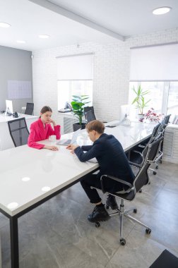 Kadın ve erkek ofiste otururken konuşuyorlar.