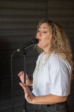 Beyaz kadın müzik stüdyosunda mikrofona şarkı söylüyor.