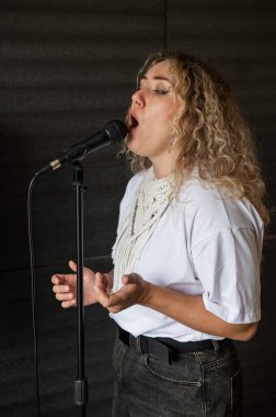 Beyaz kadın müzik stüdyosunda mikrofona şarkı söylüyor.