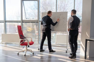 Beyaz bir kurulda iş tartışan iki beyaz adam.