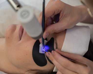 Kirpik uzatma prosedüründen geçen bir kadın ultraviyole lamba kullanıyor.