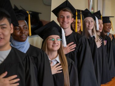 Mezunlar törende gururla dururlar. Elleri kalplerinin üstünde.