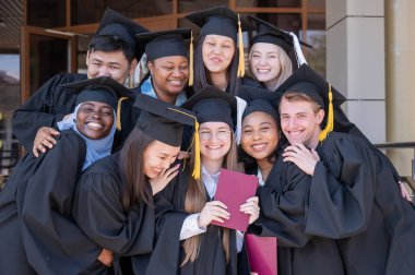Farklı uluslardan mutlu öğrenciler mezuniyet elbiseleriyle diplomalarını tutuyorlar.