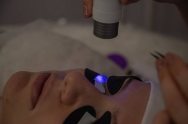 Kirpik uzatma prosedüründen geçen bir kadın ultraviyole lamba kullanıyor.