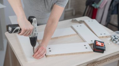 Beyaz bir kadın dolap monte ederken vidayı sıkmak için tornavida kullanıyor.
