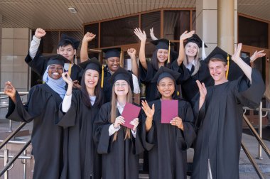 Farklı uluslardan mutlu öğrenciler mezuniyet elbiseleriyle diplomalarını tutuyorlar.