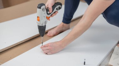 Beyaz bir kadın dolap monte ederken vidayı sıkmak için tornavida kullanıyor.
