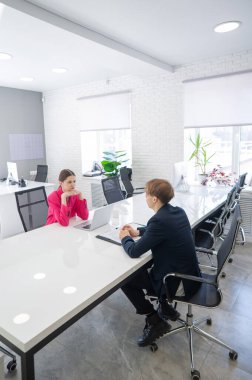 Kadın ve erkek ofiste otururken konuşuyorlar.