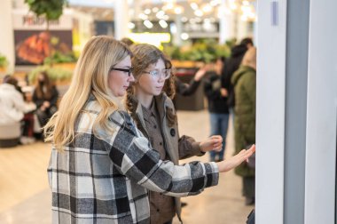 Bir anne ve genç kızı bir alışveriş merkezinde yürüyorlar.