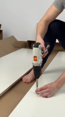 Beyaz bir kadın dolap monte ederken vidayı sıkmak için tornavida kullanıyor.