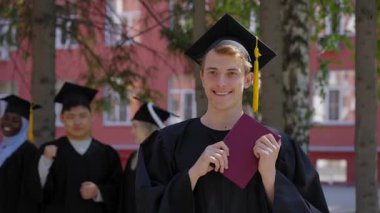 Sınıf arkadaşları onu alkışlarken elinde diploma tutan genç beyaz bir adam.