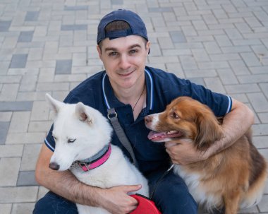 Bir adam yürürken iki köpeğini kucaklıyor.