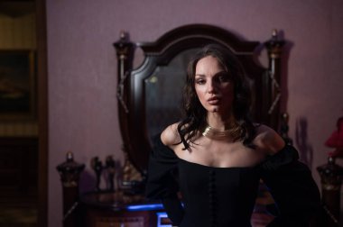 Siyah bir gece elbisesi içindeki güzel bir esmer eski tarz bir aynanın önünde poz veriyor.