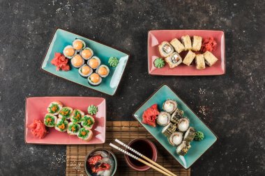 Şefin karanlık arka planda servis ettiği birkaç tabak suşi rulosu. Bir kopya alanı ile yukarıdan görüntüle. Restoran yemeği. Düz yatıyordu