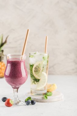 İki bardak içki, taze böğürtlenlerden yapılmış bir smoothie ve hafif arkaplanlı limonlu ve naneli mojito. Kopyalama alanı ile yan görünüm. Restoran yemekleri..