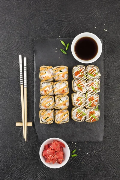 Japanese sushi on a dark background. Sushi rolls set of two types with pickled ginger, soy sauce and chopsticks. Top view with copyspace. Asian or Japanese cuisine.