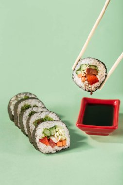 Parlak yeşil bir arka planda soya sosu için tabak ile taze sebzeli rulo, metin için bir kopya alanı ile yan görünüm. Sağlıklı bir diyet için vejetaryen suşi ruloları. Asya yemekleri popülerdir..