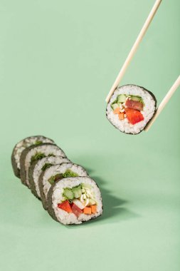 Parlak yeşil arka planda çubuklu taze sebzeli rulo, metin için bir kopya alanı olan yan görüş. Sağlıklı bir diyet için vejetaryen suşi ruloları. Asya yemekleri popülerdir..