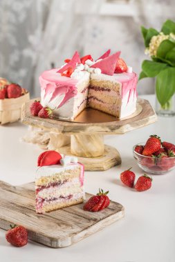 Çilek dolgulu bisküvi keki ve arka planda tahta bir tezgahta kesilmiş taze çilek. Metin için bir kopya alanı ile yan görünüm. Tatil ve doğum günü için tatlı..