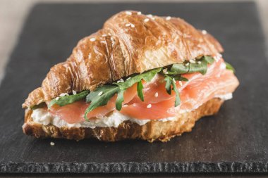 Siyah tahta üzerinde somon, ricotta peyniri ve roka kaplı kruvasan sandviçi. Yakın plan. Yatay yönelim.