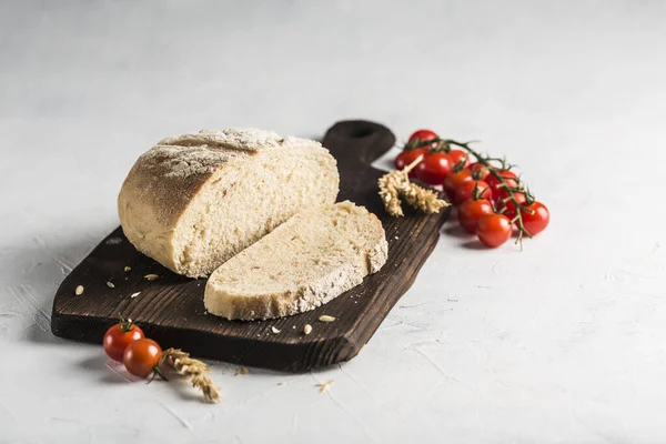 Bread with dried tomatoes on a dark wooden board on a light background. Fresh baked products for healthy nutrition. Side view with a copy space for the text.
