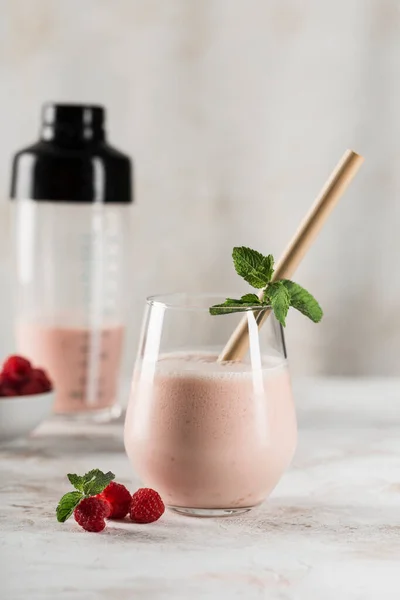 A glass with a Lassi drink with raspberries, mint, a bamboo tube and a cocktail shaker on a light background. Vertical orientation. Side view. Indian traditional refreshing drink.