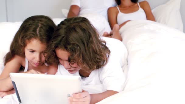 Jolis frères et sœurs utilisant la tablette sur leur lit de parents — Video