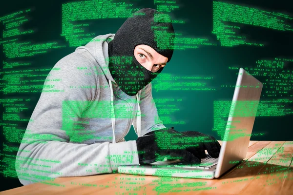 Focused thief with hood typing on laptop — Stock Photo, Image