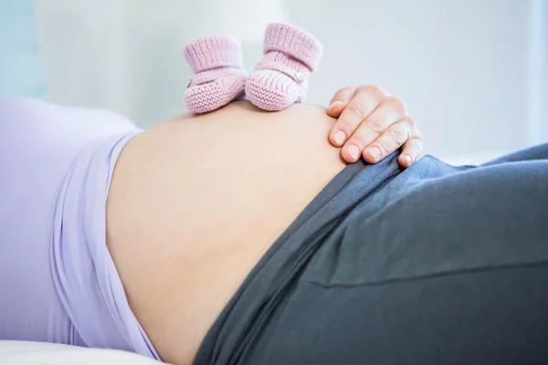 Těhotná žena s baby boty na břicho — Stock fotografie