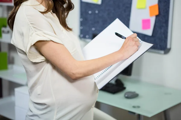 Donna d'affari incinta che scrive in cartella — Foto Stock
