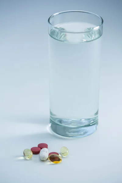 Pills beside glass of water — Stock Photo, Image