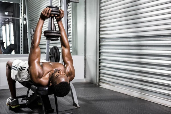 Shirtless man lifting dumbbell on bench — Stock Photo, Image