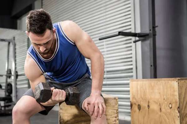 Muscular man lifting dumbbell on wooden block — Stock Photo, Image