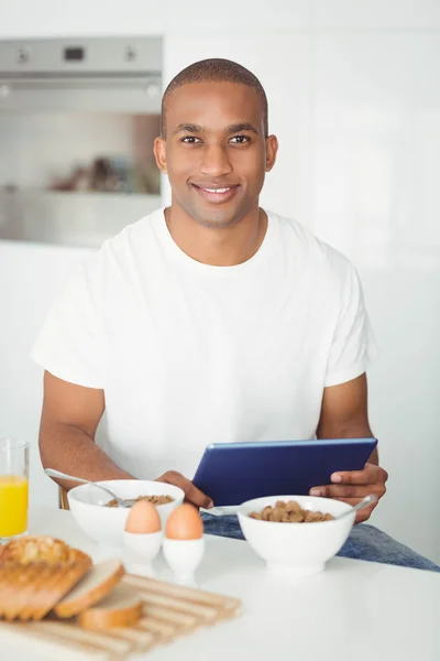 Jeune homme utilisant tablette et petit déjeuner dans la cuisine — Photo