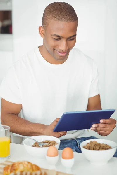 Hombre joven usando la tableta y desayunando en la cocina —  Fotos de Stock