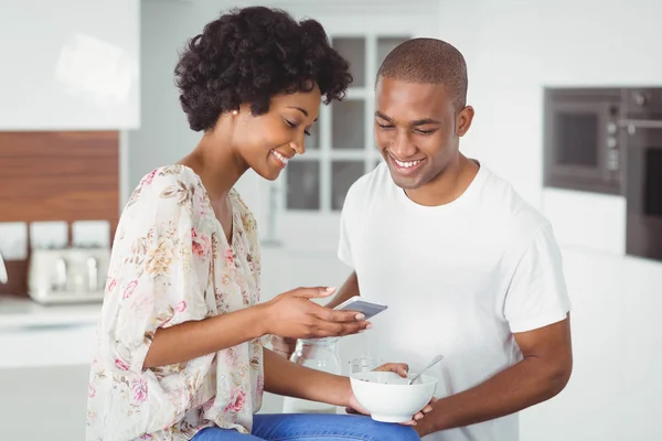 Happy couple eating breakfast and using smartphone — ストック写真