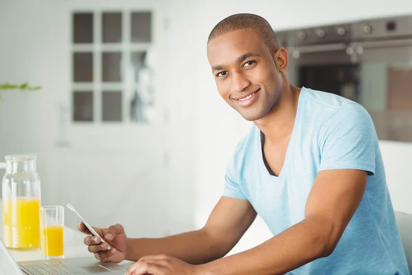 Uśmiechnięty człowiek za pomocą laptopa i smartfona — Zdjęcie stockowe