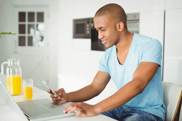 Homme souriant utilisant un ordinateur portable et un smartphone — Photo