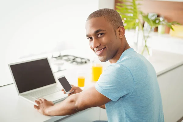 Homme souriant utilisant un ordinateur portable et un smartphone — Photo